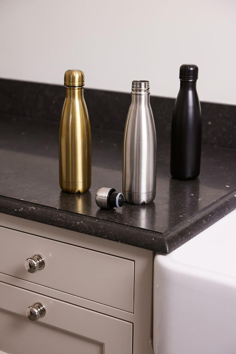 Tre stålflaskor i guld, silver och svart på köksbänk, en avskruvad lock bredvid
