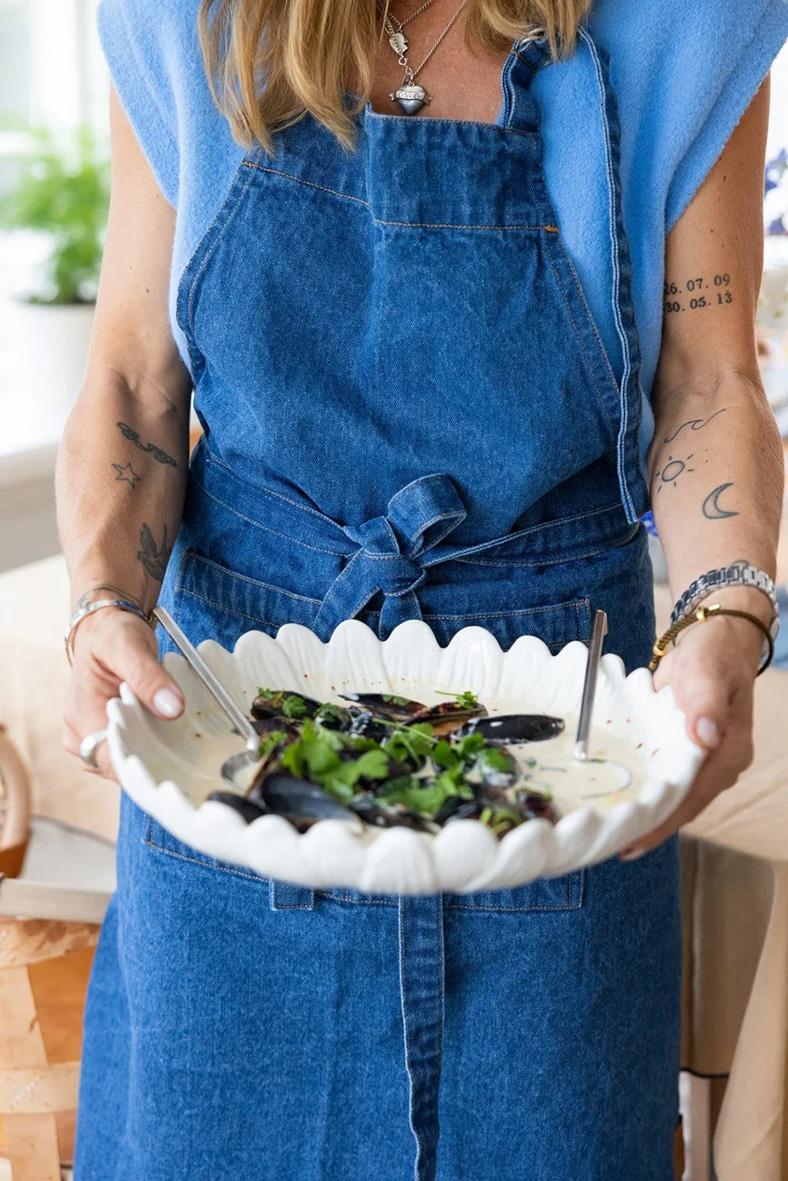 Person i blå denim förkläde som håller en stor skål med musslor
