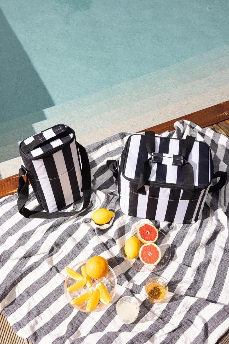Kylväska Sagaform City Retur Pet Hög Svart/Vit med frukt och drycker på en strandhandduk