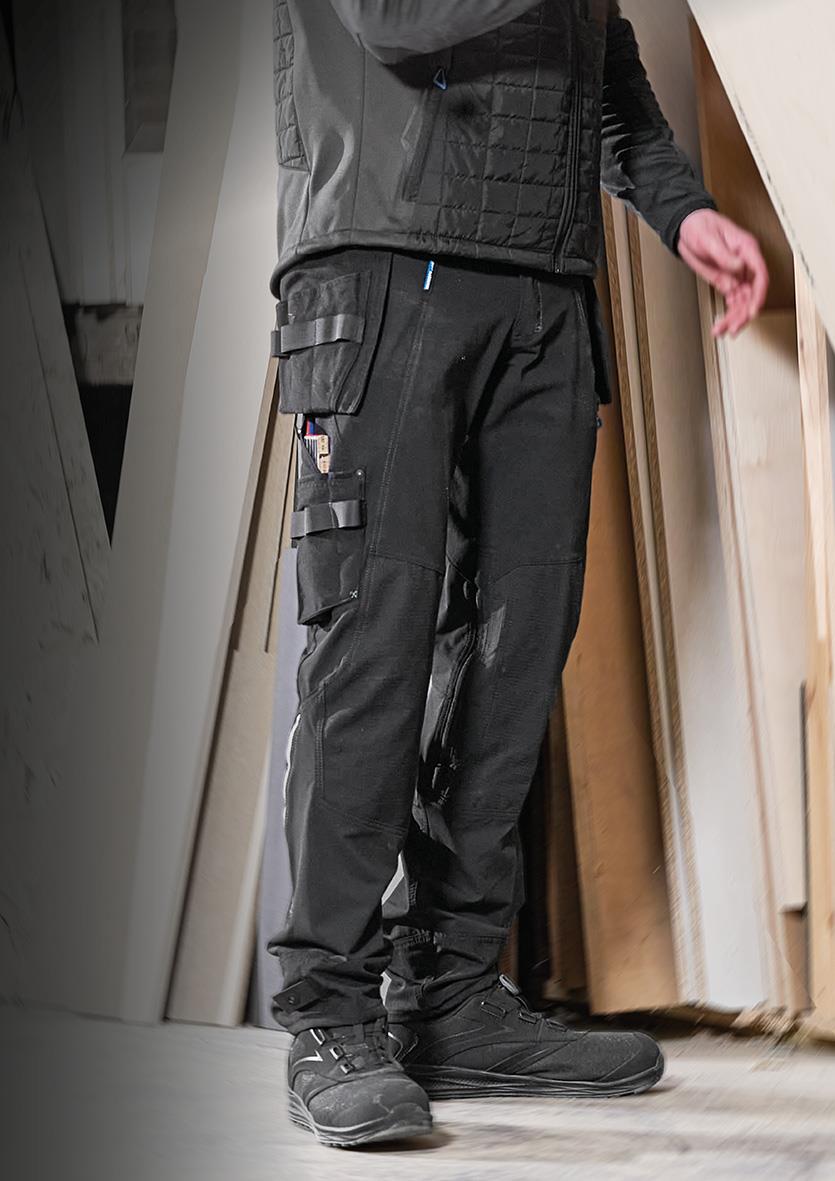 Person i svart hantverksbyxa och svart jacka står inomhus, visar arbetskläder