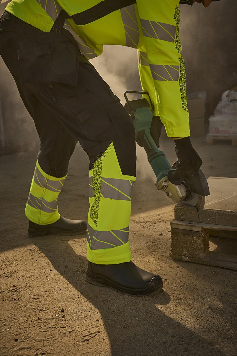 Person i svarta och varselgula hantverksbyxor använder vinkelslip för att skära i trä på byggarbetsplats