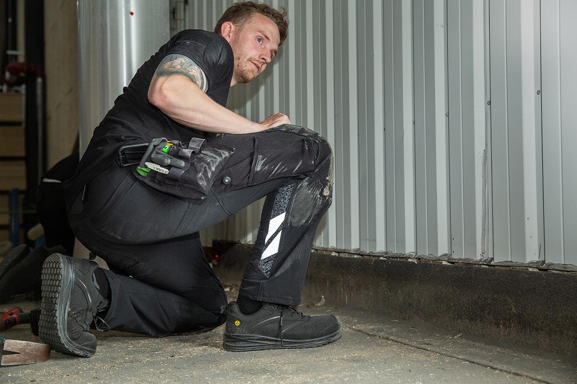 Man i svart hantverksbyxa knäböjer vid en metallvägg
