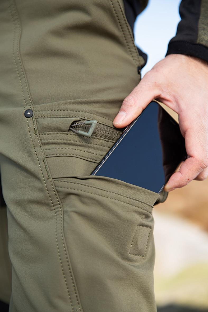 Person som bär mossgrön och svart unisex midjebyxor med telefon i fickan