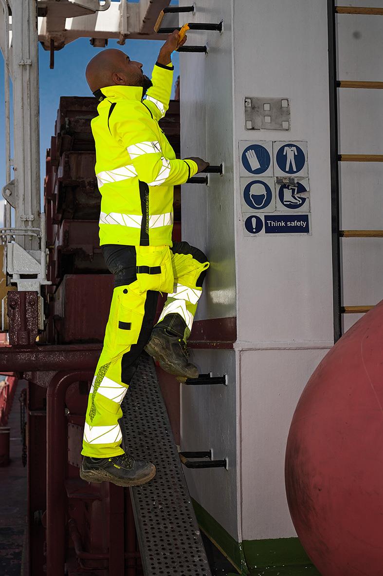 Person i högsynkade västbyxor klättrar på en vägg med säkerhetsutrustning i industriell miljö