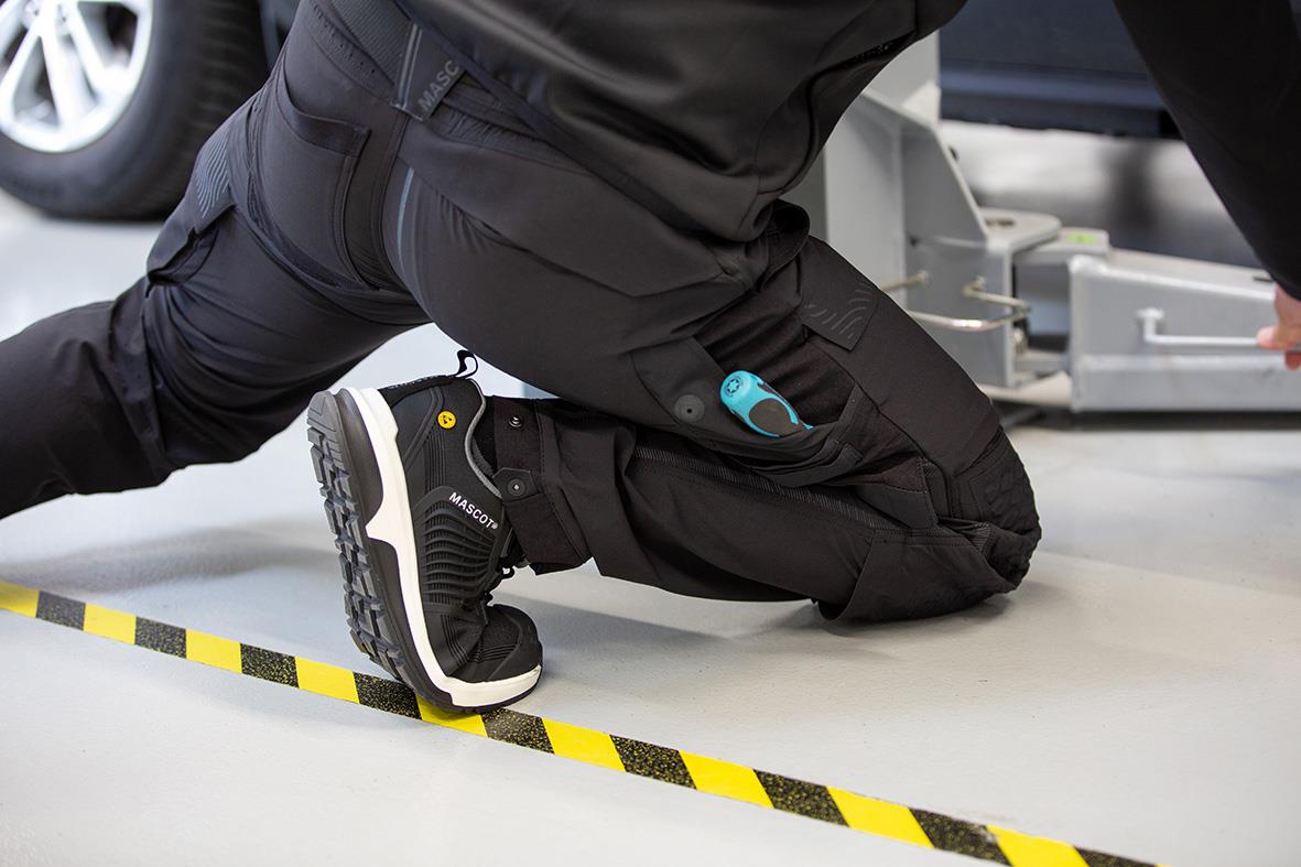 Person som knäböjer på golvet i svarta arbetskläder, nära en gul och svart avspärrningsremsa