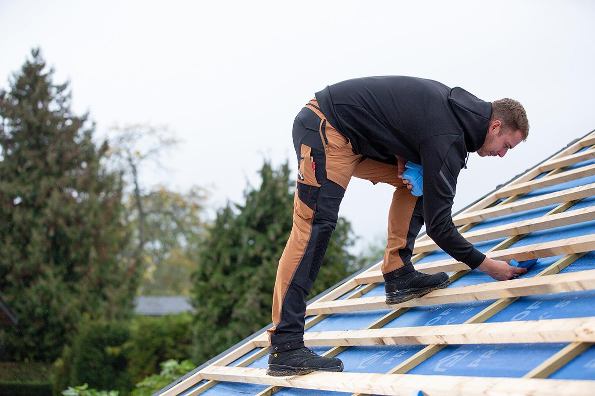 Man som arbetar på ett tak med träreglar och blå plastfolie utomhus