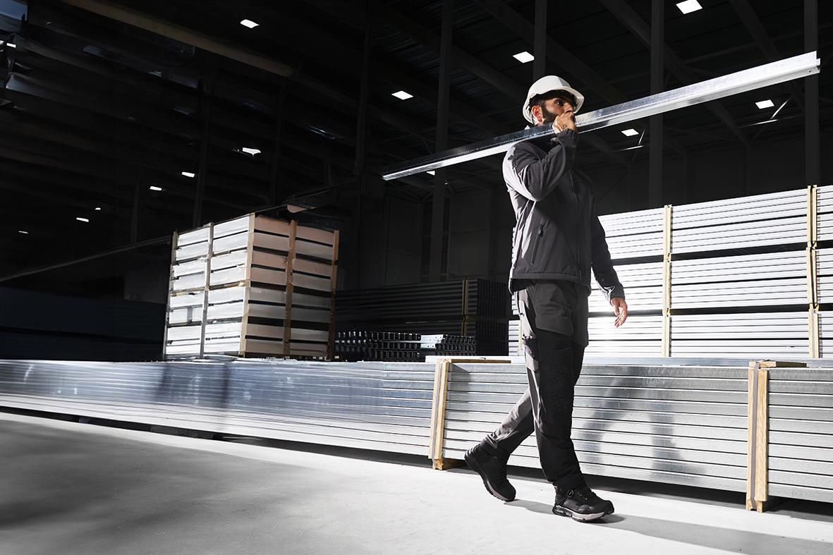 Person i svart jacka och hatt går i en industriell miljö med lagerhyllor och belysning