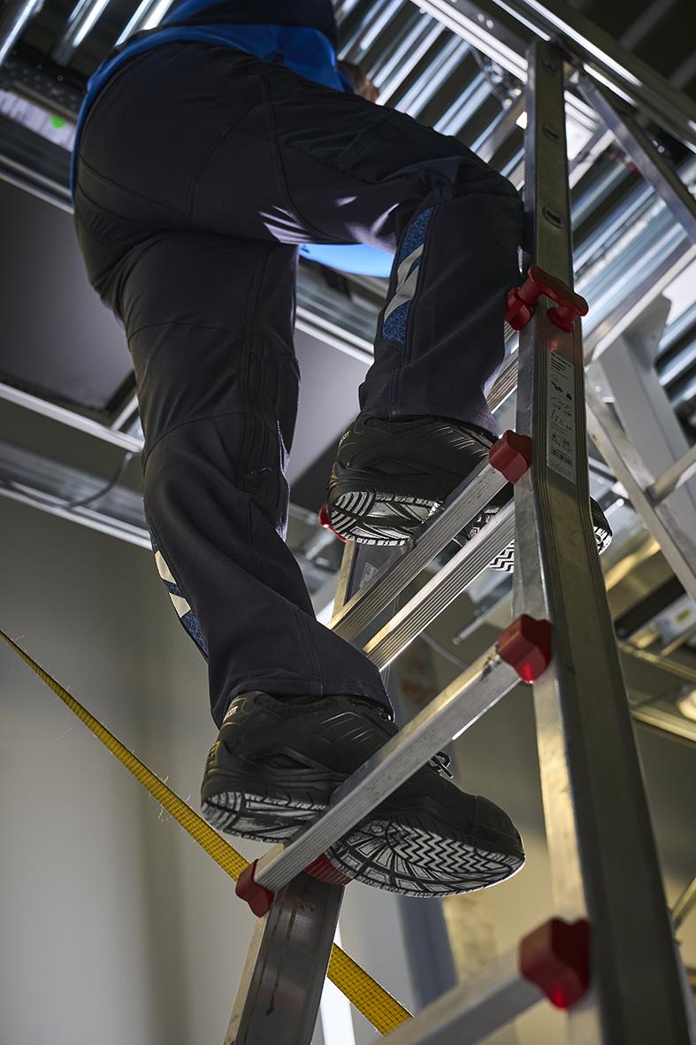 Person klättrar uppför en stege i en industriell miljö, sätter foten på stegens steg