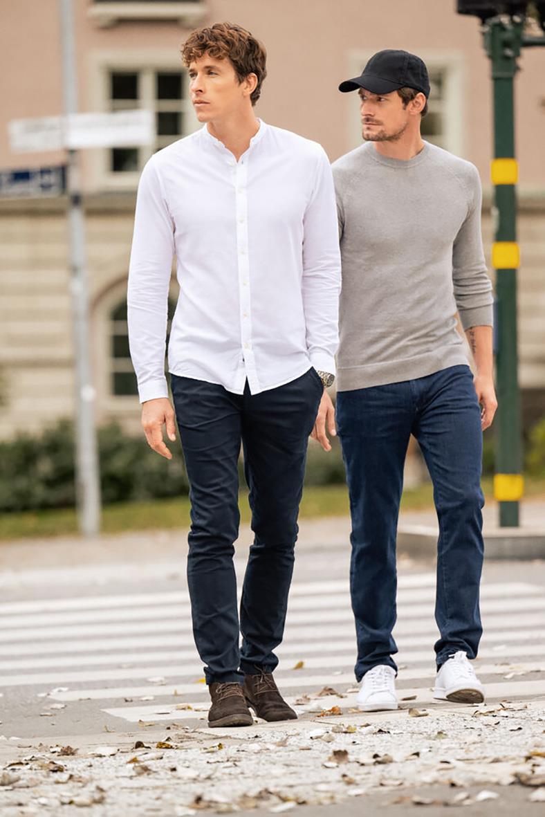 Två unga män promenerar på en stadsgata, en i vit skjorta och den andra i grå tröja och svart keps