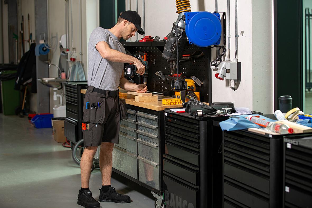 Man i verkstad arbetar med verktyg och maskiner, omgiven av arbetsbänkar och förvaringsskåp