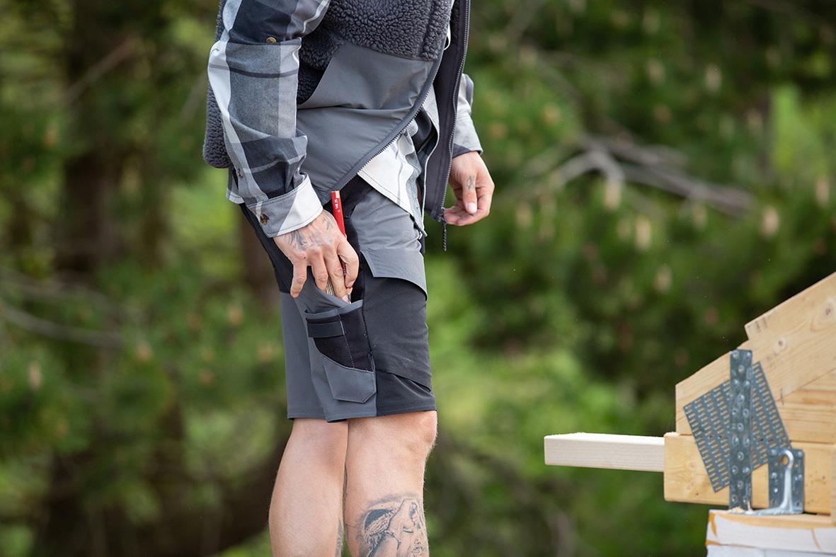 Person som bär svarta och grå shorts med stretchmaterial, utomhus med träd i bakgrunden