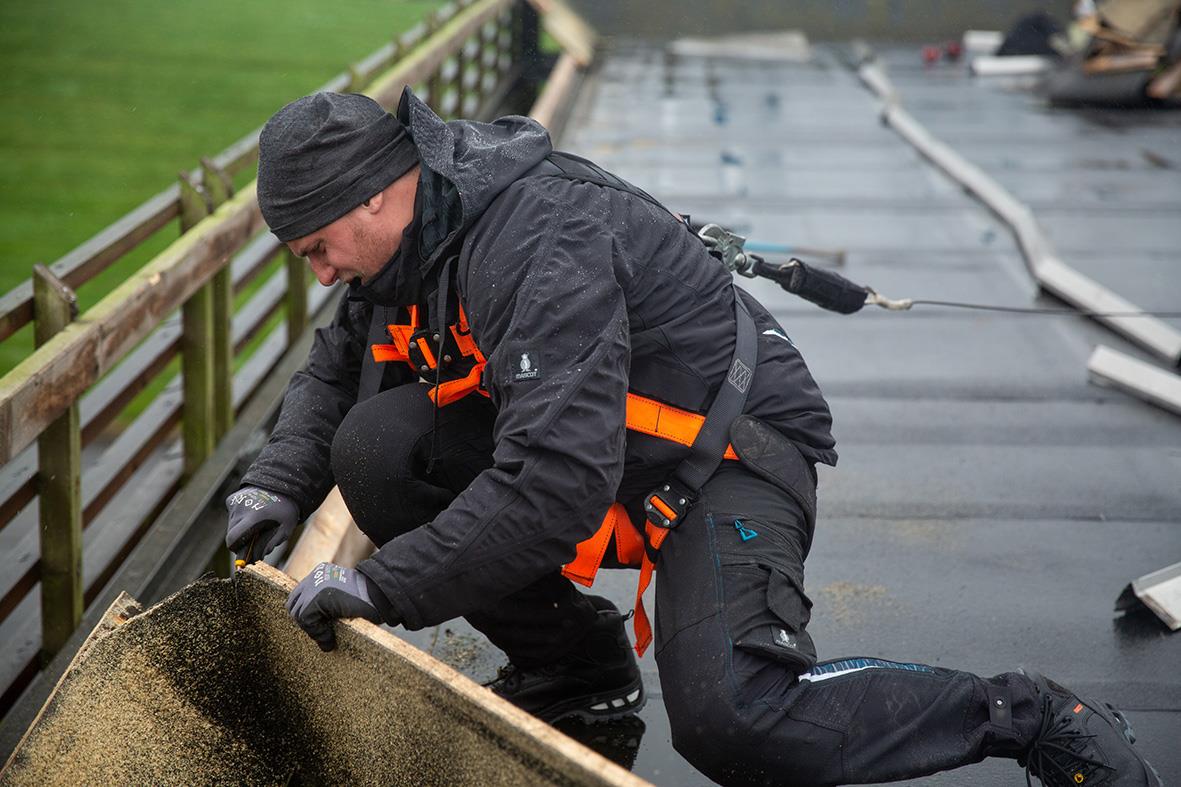 Person i svart vinterjacka och byxor arbetar på tak, använder säkerhetsutrustning