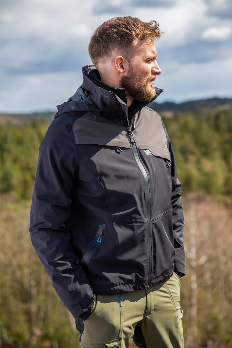 Man i svart och grå skaljacka utomhus med natur i bakgrunden