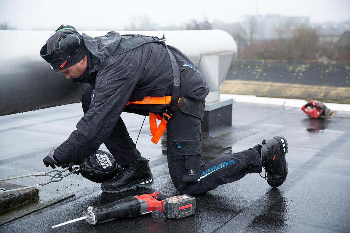 Person som arbetar på tak med verktyg, vinterjacka och säkerhetsutrustning