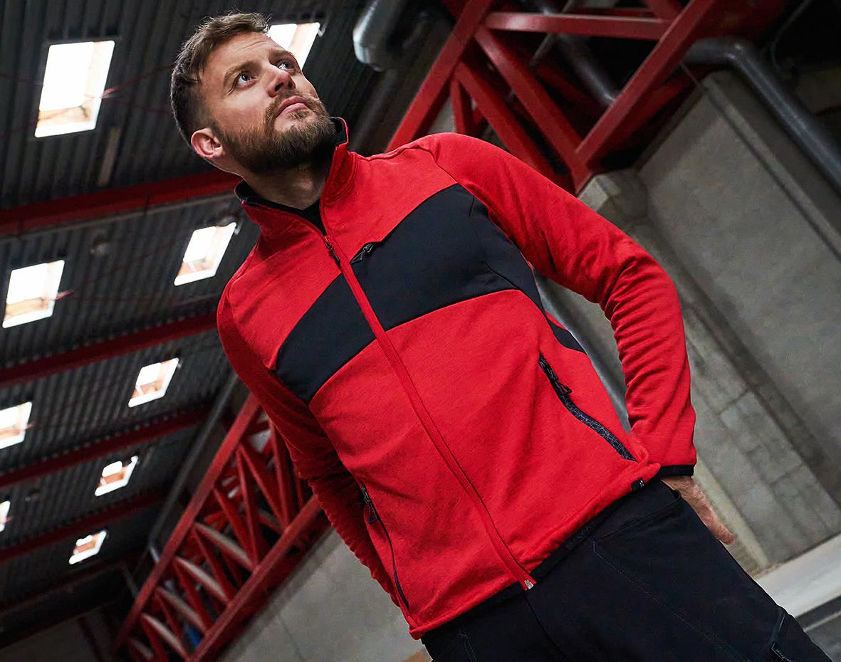 Man i röd fleecejacka med svart band över bröstet, stående i industrimiljö