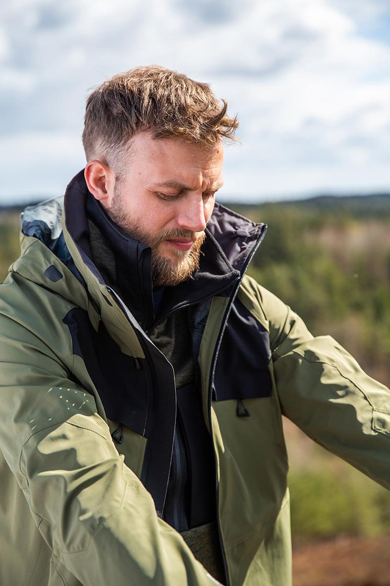 Man i stretch mossgrön/svart skaljacka med huva, utomhus i naturen