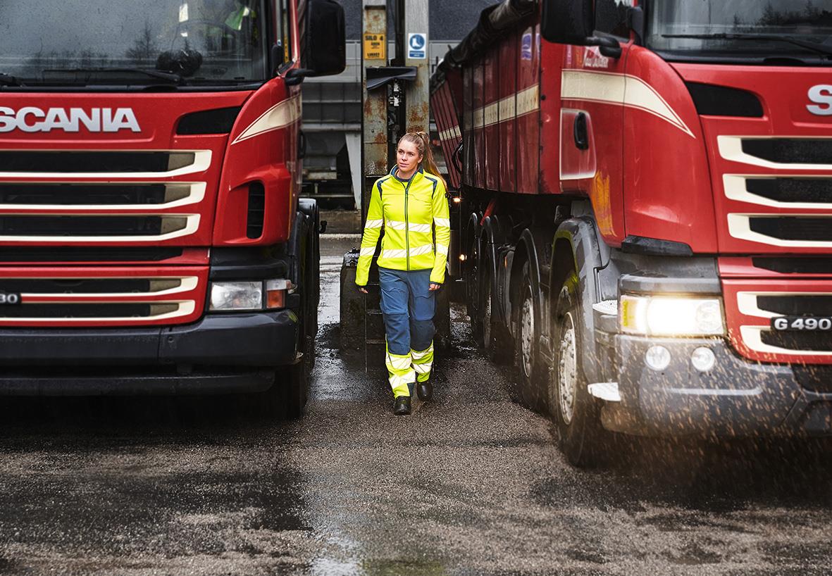 Person i reflexväst mellan två stora lastbilar på våt väg