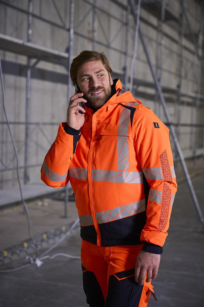 Man i orange varseljacka med reflexdetaljer, stående i byggarbetsmiljö