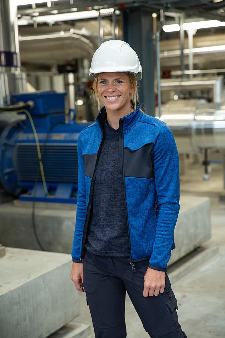 Kvinna i blå fleecetröja och vit hjälm i industrimiljö