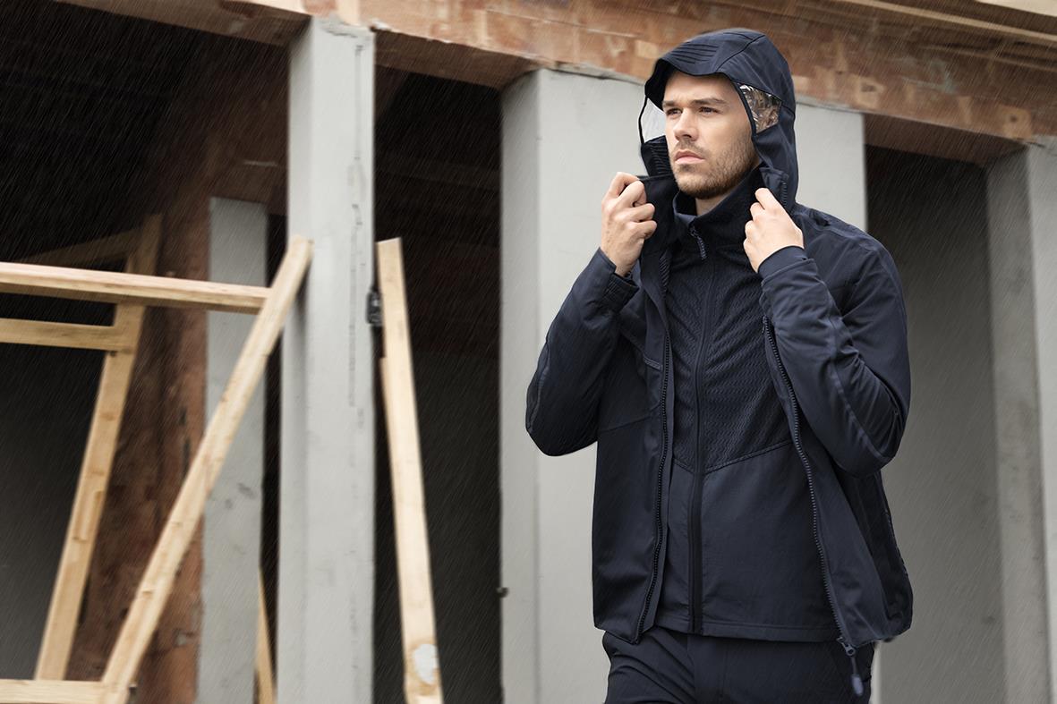 Man bär mörk marin skaljacka med huva på byggarbetsplats