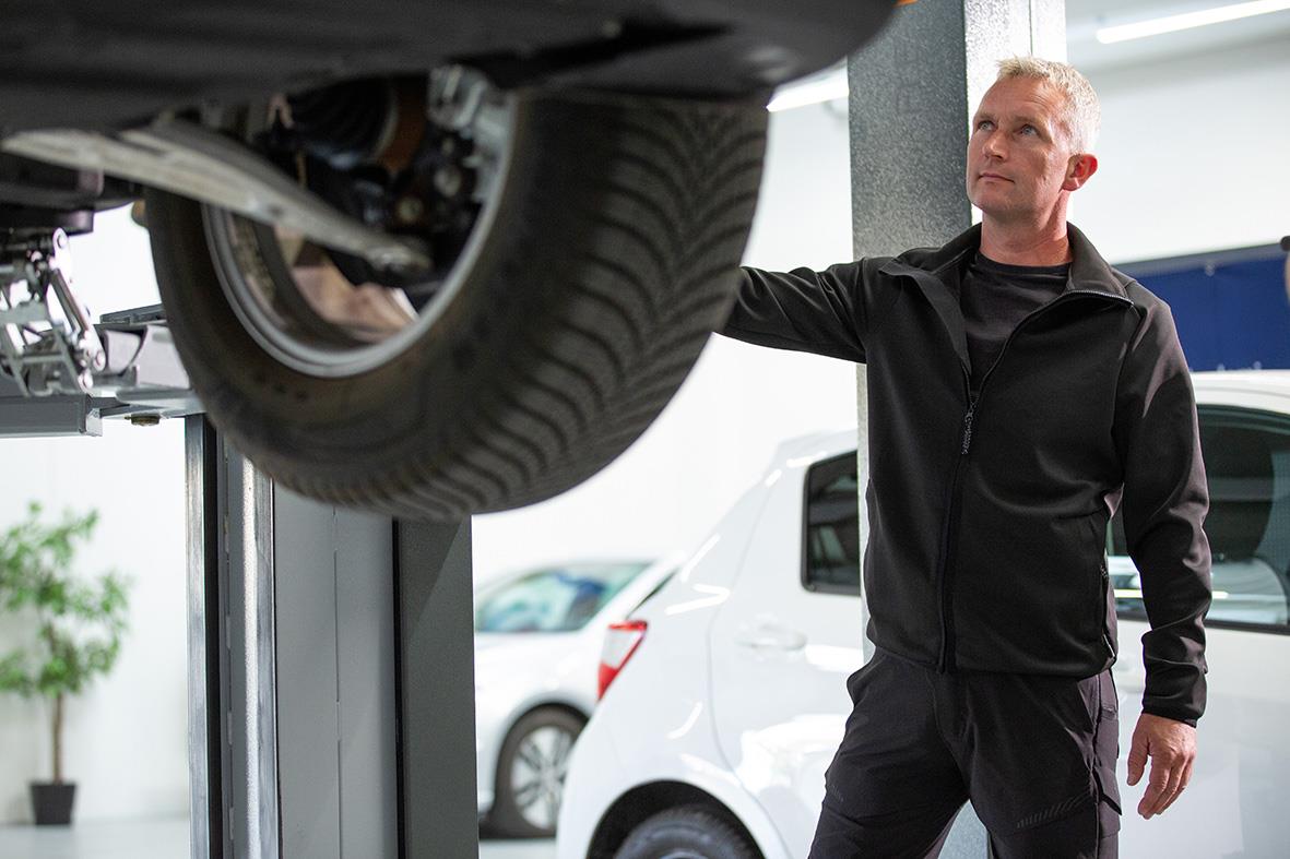 Man i svart fleecejacka under billyft i verkstad