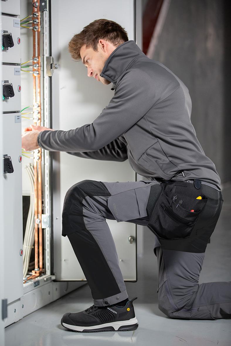 Man i grå fleecejacka som arbetar med elutrustning, knästående och justerar kablar