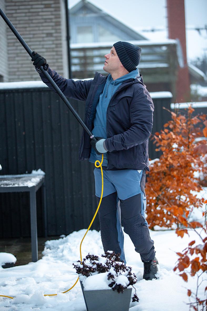 Man i vinterjacka och mössa sköter snöre utomhus på vintern med snö och buskar i bakgrunden