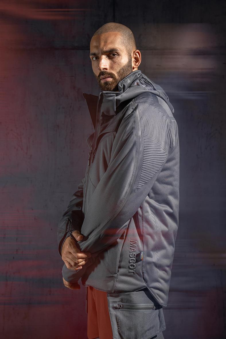 Man i grå vinterjacka Mascot 22035-657 2XL står mot mörk bakgrund