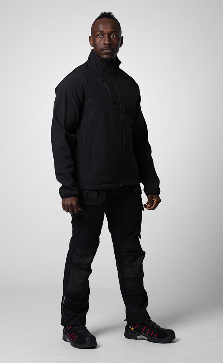 Man i svart softshelljacka och byxor står mot en ljus bakgrund