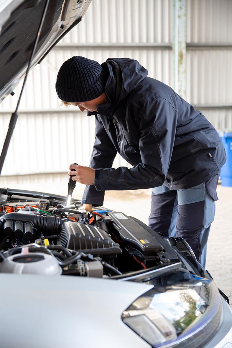 Person som kontrollerar bilmotor i en garage eller verkstad, vinterjacka och mössa