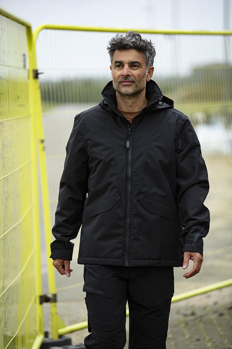 Man i marinblå vinterjacka utomhus framför gul staket