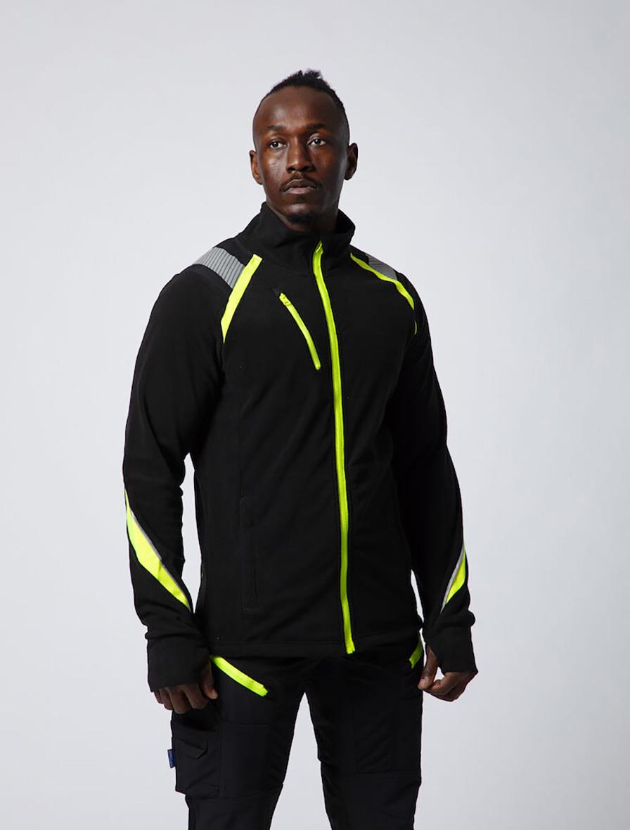 Man i svart och gul microfleecejacka med reflexdetaljer, stående pose mot ljus bakgrund