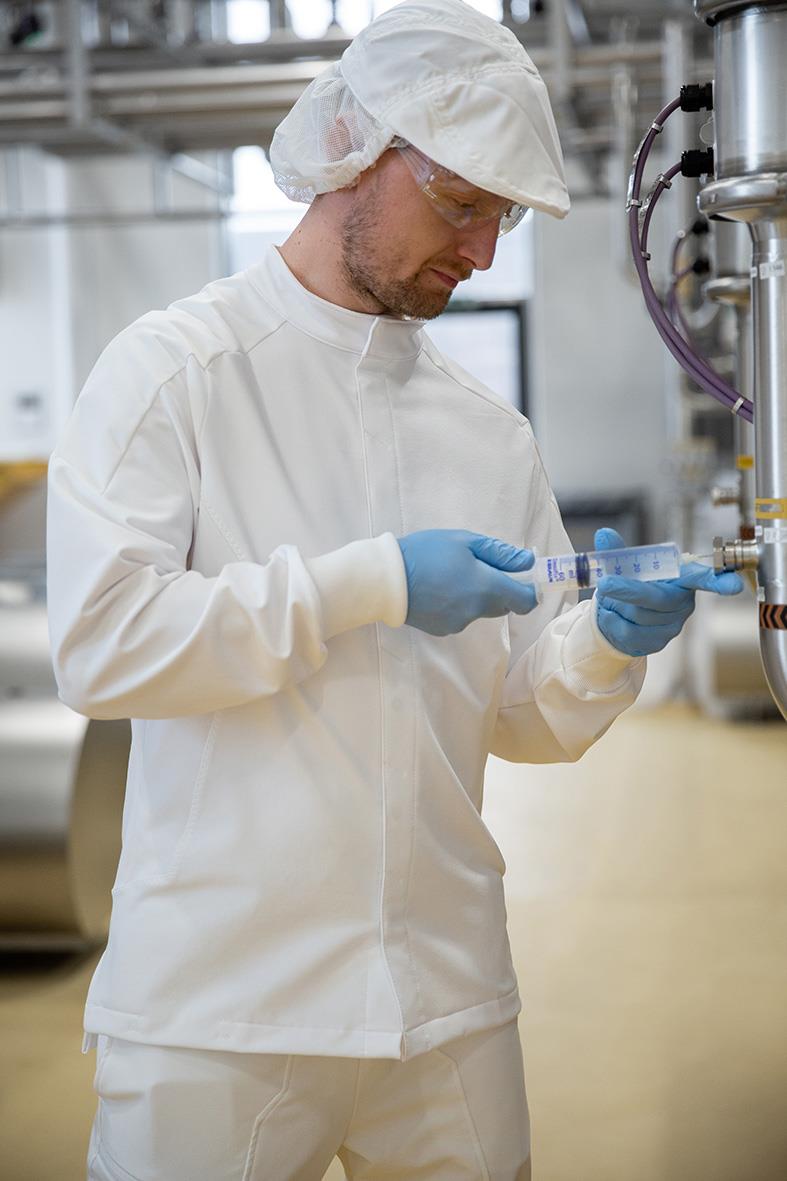 Person i labbkläder och skyddsglasögon hanterar provrör i ett laboratorium