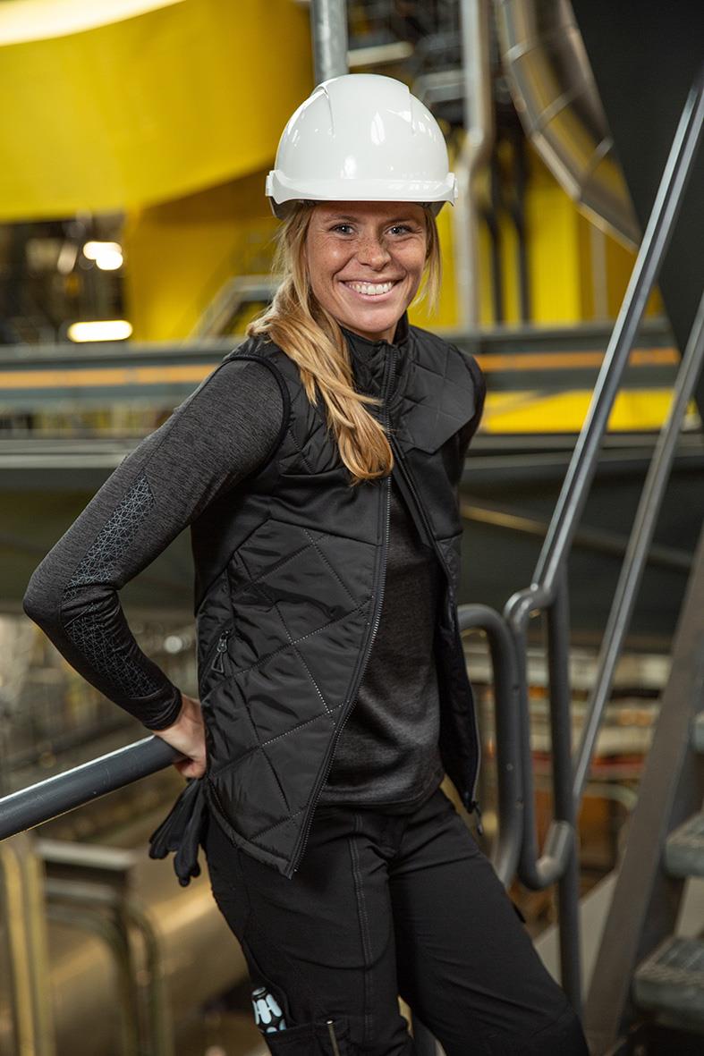 Kvinna i svart arbetsväst och vit säkerhetshjälm i industriell miljö