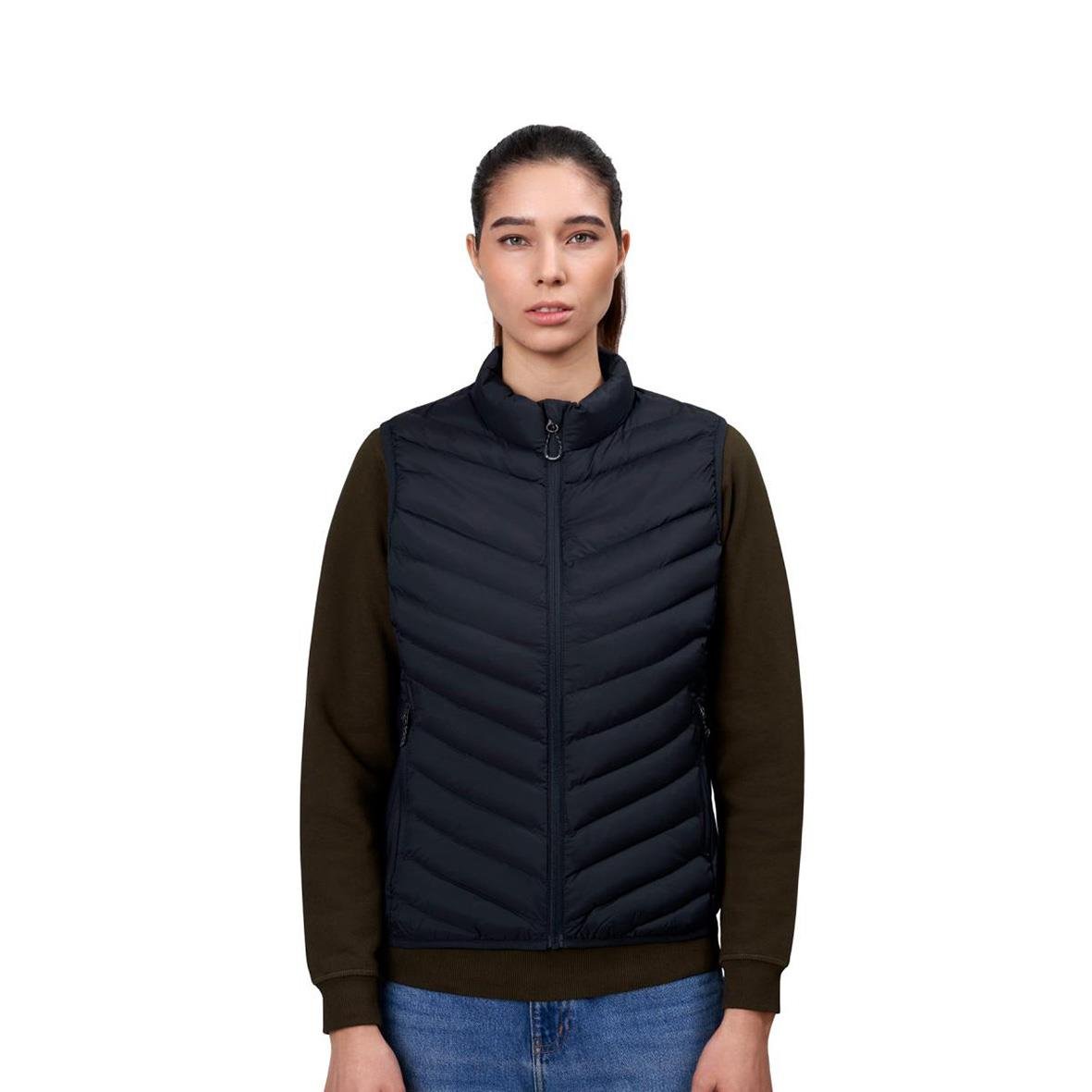 Kvinna i marin och svart väst med bruna ärmar och blå jeans, stående mot vit bakgrund