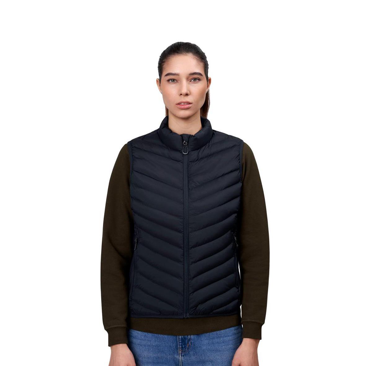 Kvinna i marin och svart väst med bruna ärmar och blå jeans, stående mot vit bakgrund