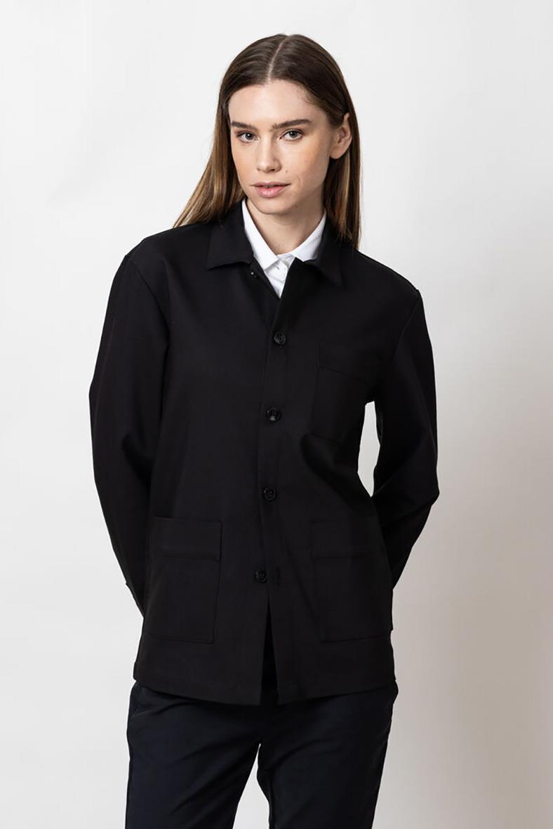Kvinna i svart overshirt med patchfickor, knappar framtill och vit skjorta under, stående pose mot ljus bakgrund