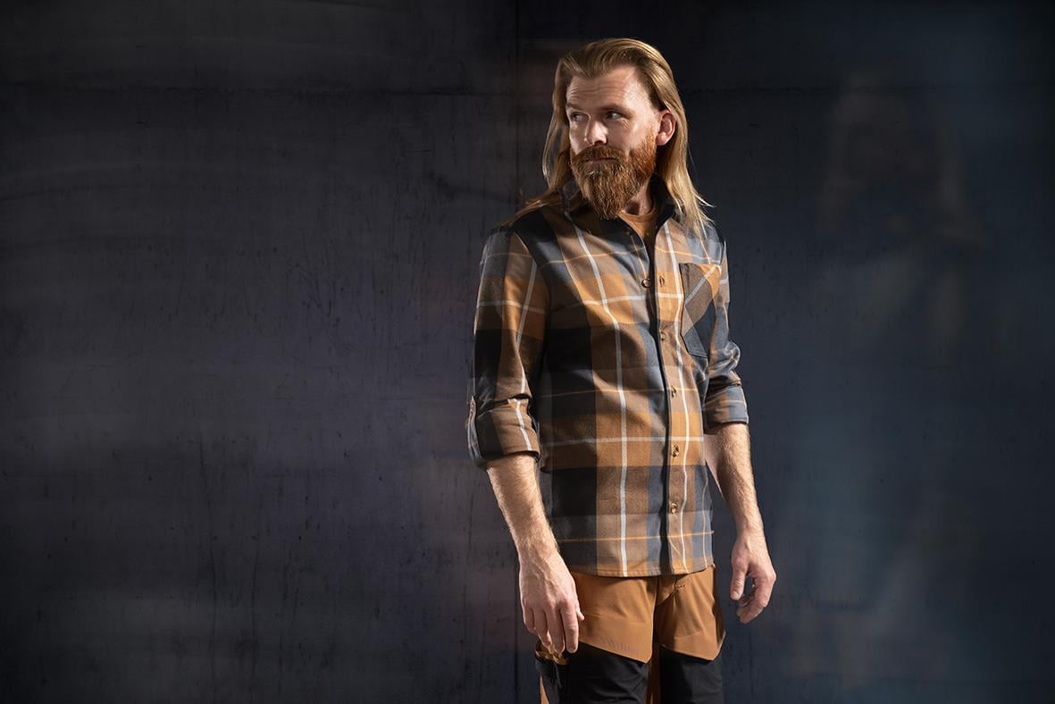 Man i brunt och svart rutiga flanellskjorta med långt ärm, stående krage, och brunt linne under