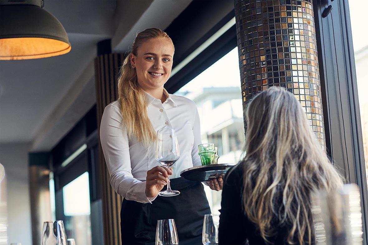 Kvinna serverar vin till en äldre kvinna i en modern restaurangmiljö