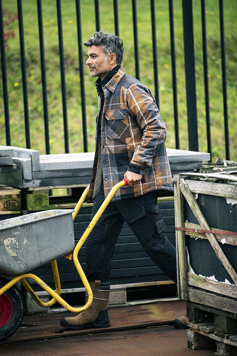 Man i flanellskjorta med rutig mönster i nötbrunt, går med en handvagn utomhus