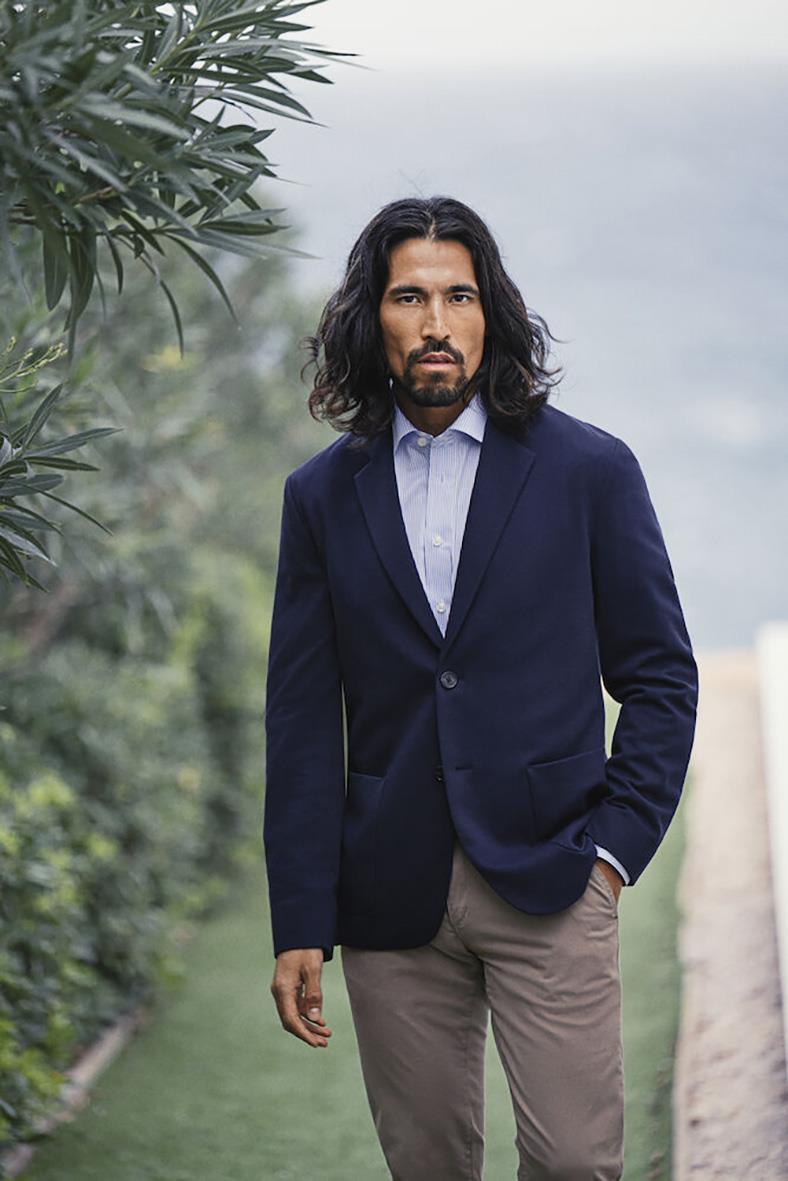 Man i marinblå casual blazer och ljusblå skjorta utomhus med grönska i bakgrunden