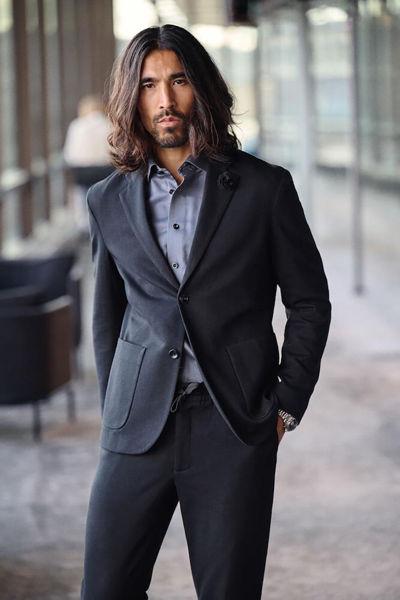 Man i mörkblå kavaj och byxor, blå skjorta, stående i modern inomhusmiljö