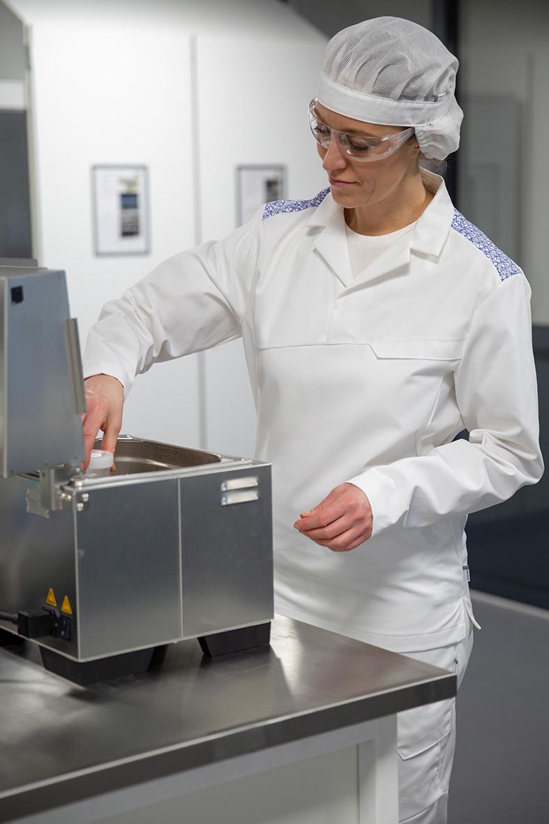 Person i vitt labb och skyddsglasögon använder laboratorieutrustning i ett modernt labbmiljö