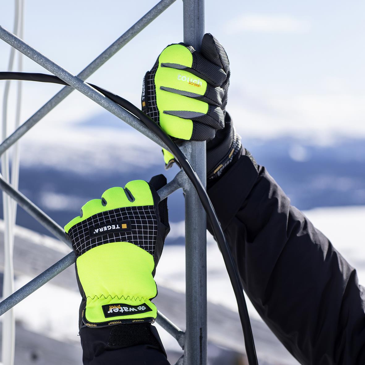 Läderhandske Tegera 9128 9 håller i ett metallstängsel utomhus i snöigt landskap