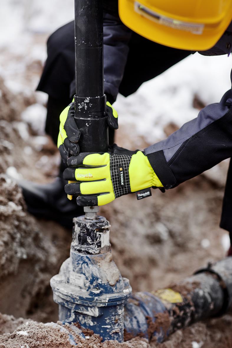 Person i arbetskläder och gula handskar arbetar med rör i marken utomhus