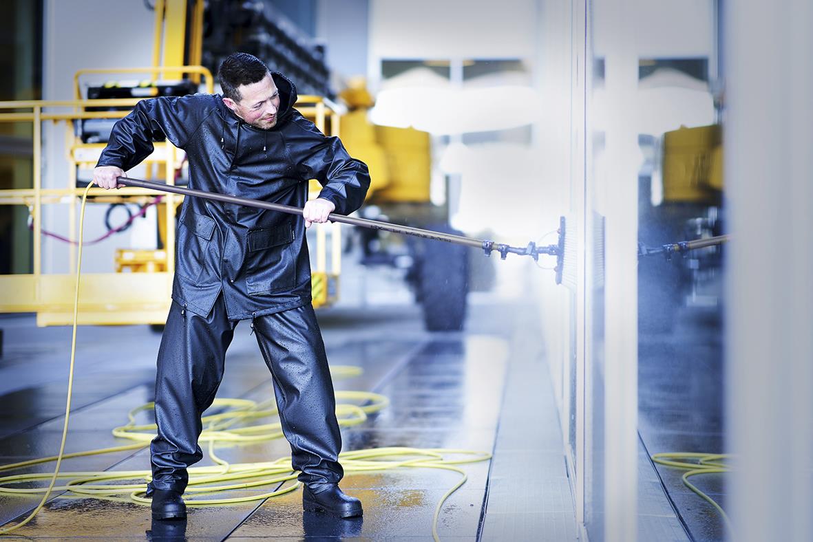 Person rengör en glasvägg med en lång borste i ett industriellt utrymme