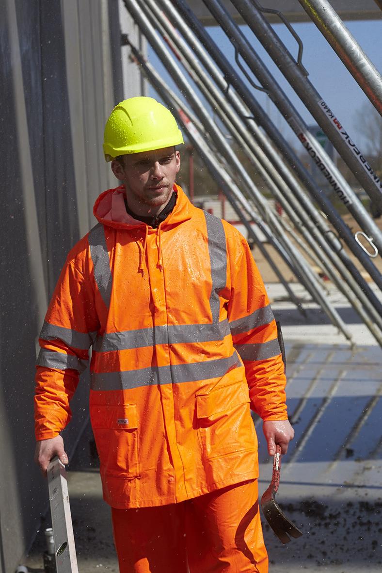 Arbetare i orange Hi-Vis regnset med reflexband, bär hjälm och håller verktyg på byggarbetsplats