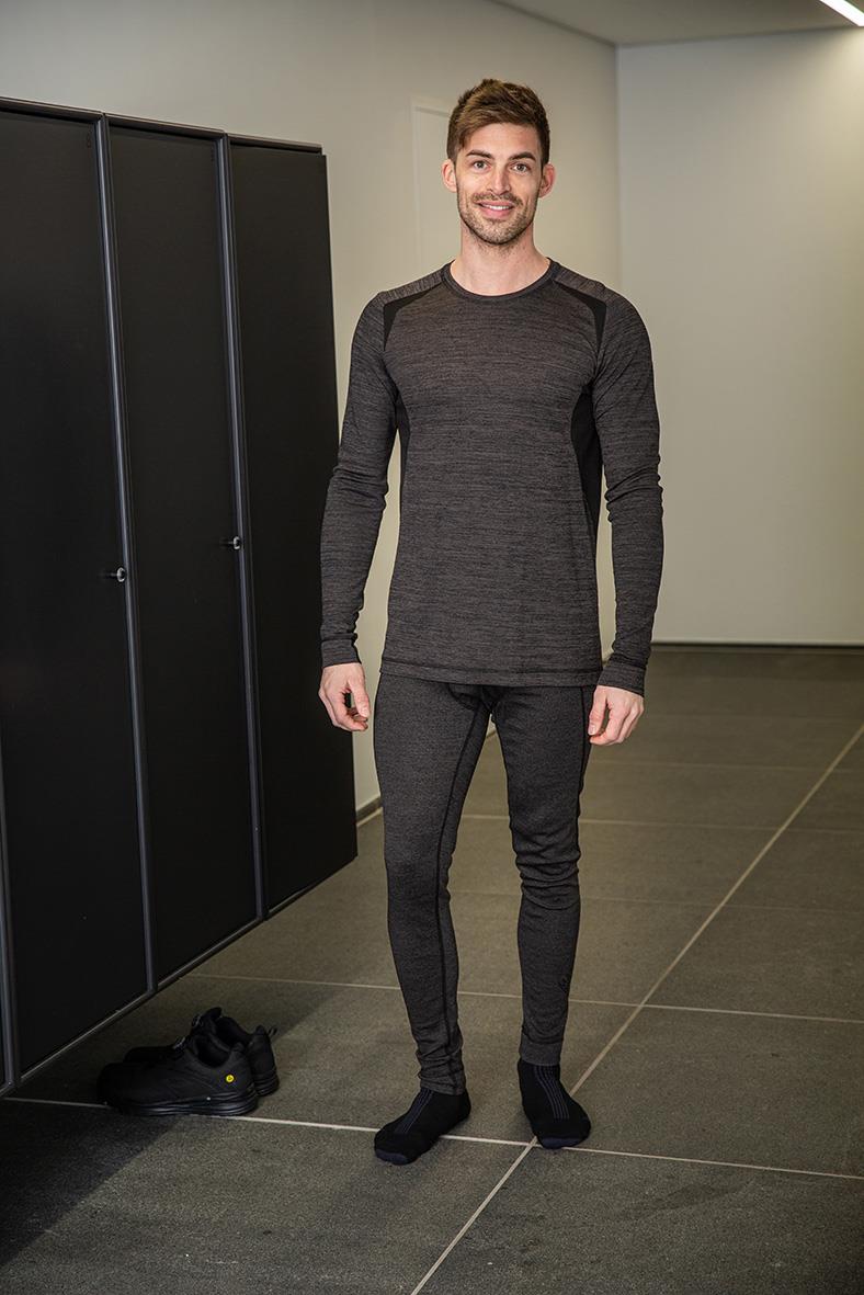 Man i mörkgrå underställströja och byxor står i ett rum med svarta skåp och grå väggar.