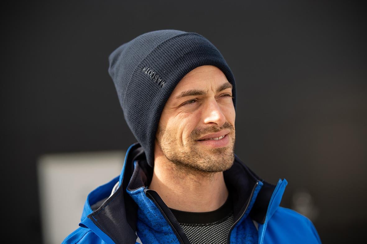 Man bär mörk marin mössa och blå jacka, ser utomhus