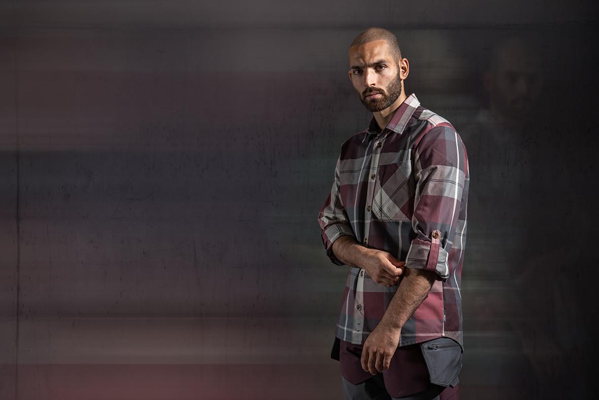 Man bär vinröd-rutig flanellskjorta med uppvikta ärmar och ser allvarlig ut